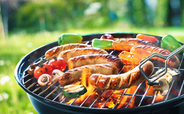 Close view of a charcoal grill with sausage and veggies being grilled on top