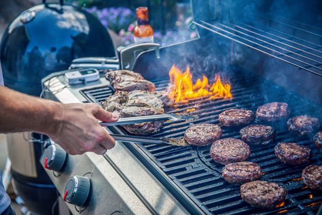 Close view of burgers and steaks being cooked on a natural gas grill