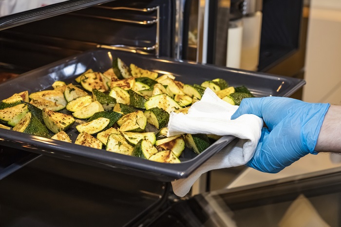 Cook takes out from the oven a sheet of the tray with fried zucchini.