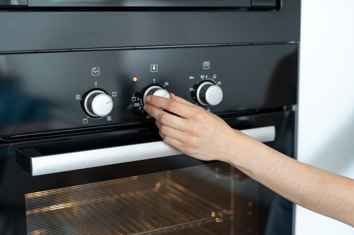 Hand adjusting the temperature knob on the oven.