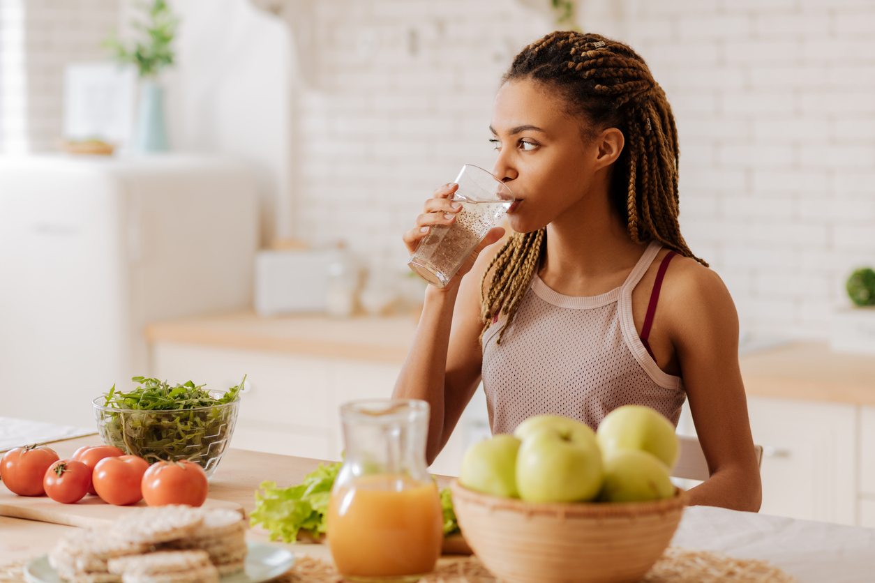 young woman drinks a glass of filtered water in her kitchen
