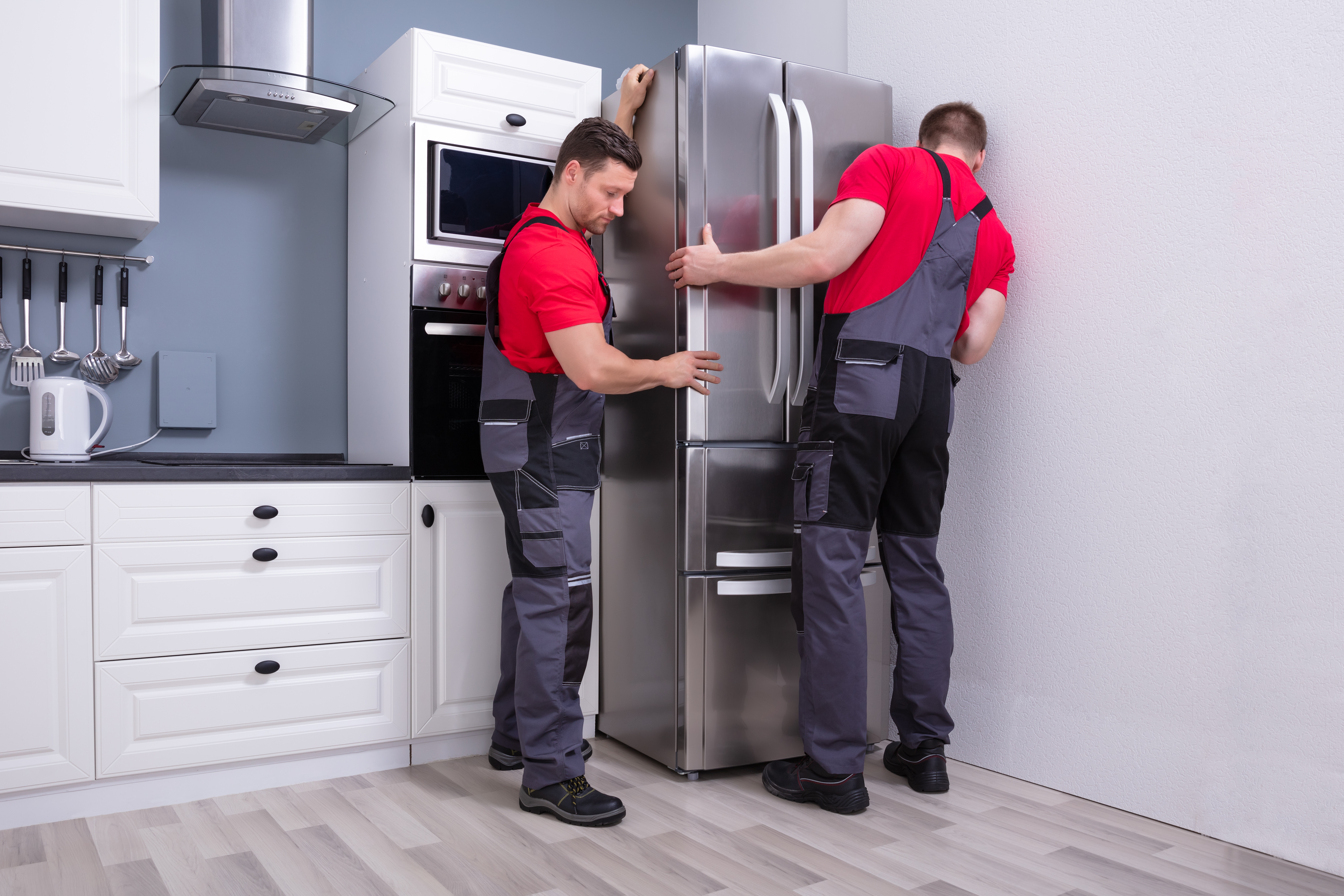 Two professional appliance installers placing a new refrigerator in a kitchen 