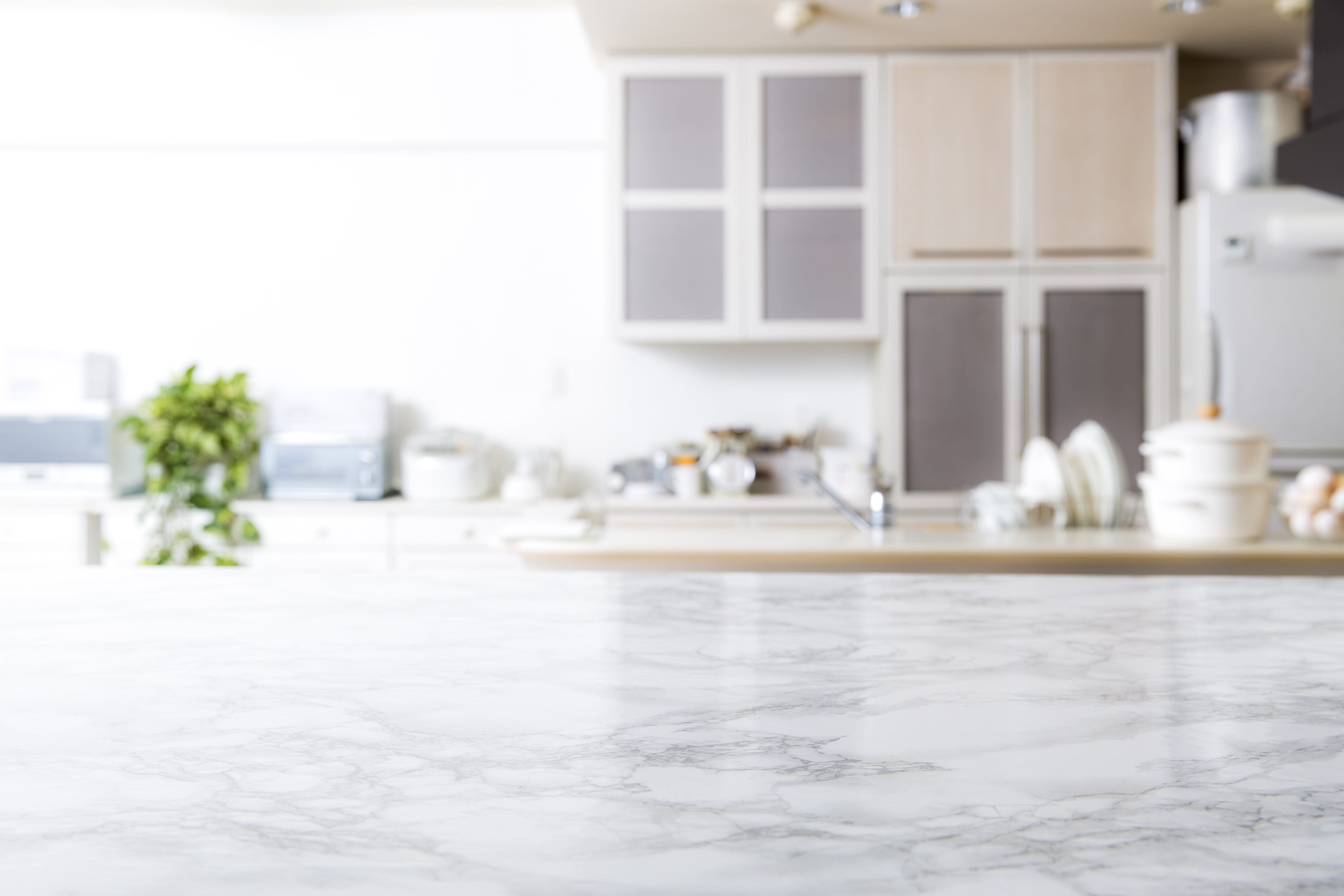 Close up of a marble countertop in the foreground with a kitchen in the background 