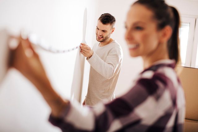 view of a man and woman measuring the length of a wall with a measuring tape