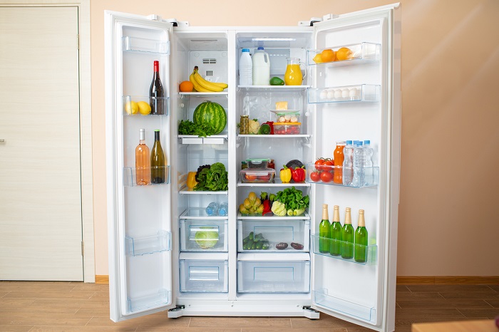 Open side by side refrigerator full of fresh fruits, vegetables, and drinks