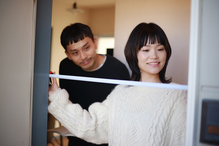 A couple measuring the width of a refrigerator space. 