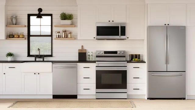 Modern kitchen with white cabinets, black countertops, and outfitted with a stainless steel Samsung appliance package including a dishwasher, electric range, microwave, and French door refrigerator. 