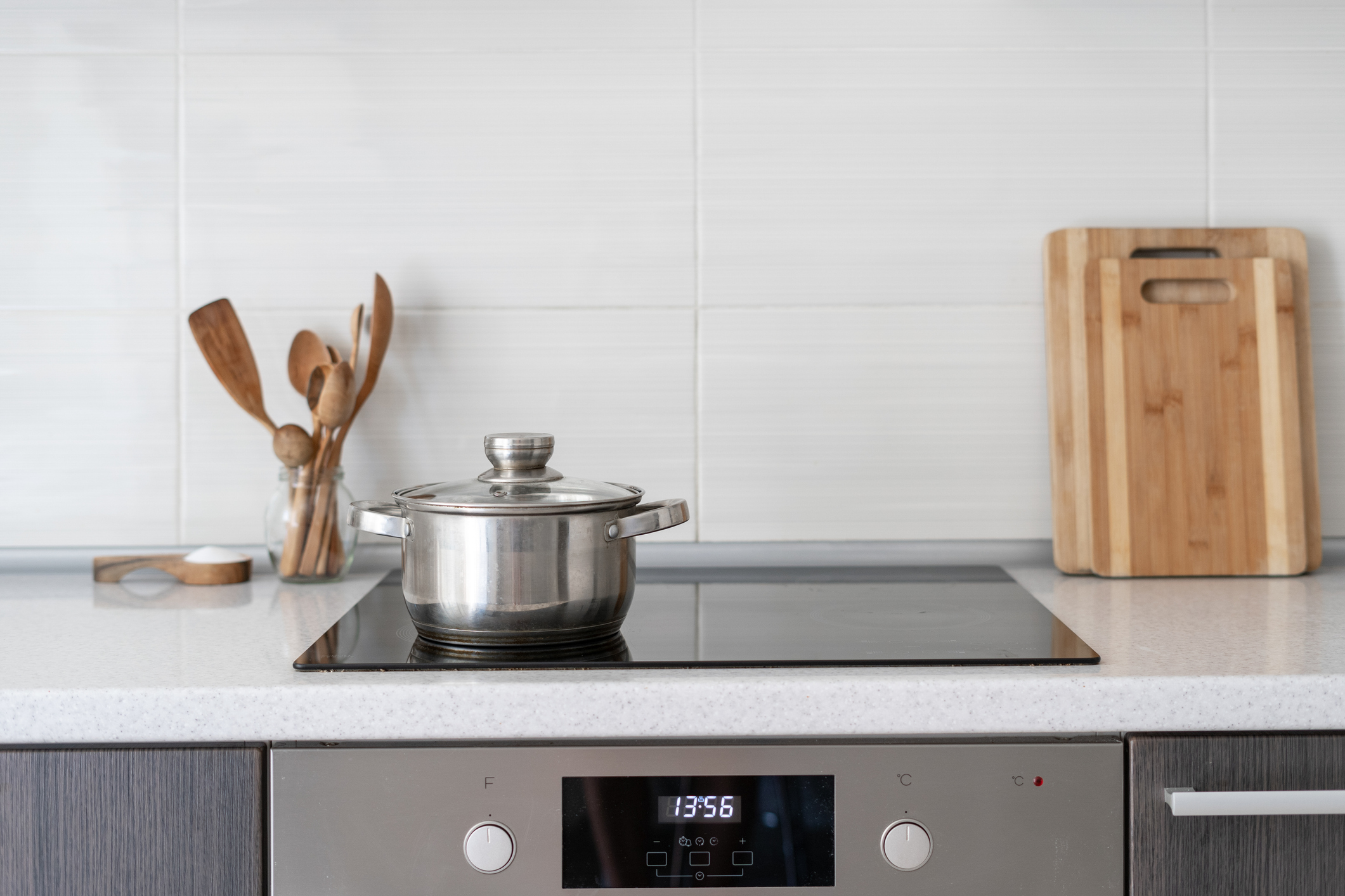 Shot of induction cooktop with small pot next to wooden utensils and cutting boards atop a counter
