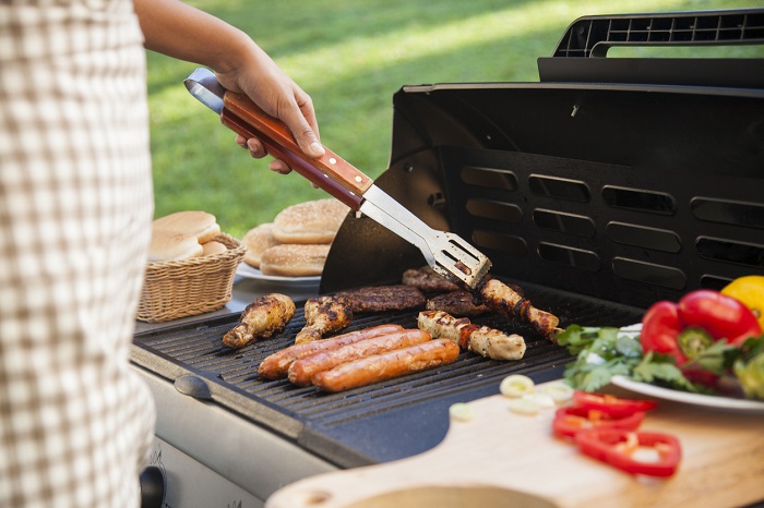Man bbqing with different meat, veggies, and more.