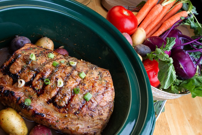 Slow cooker with roast inside and veggies on side. 