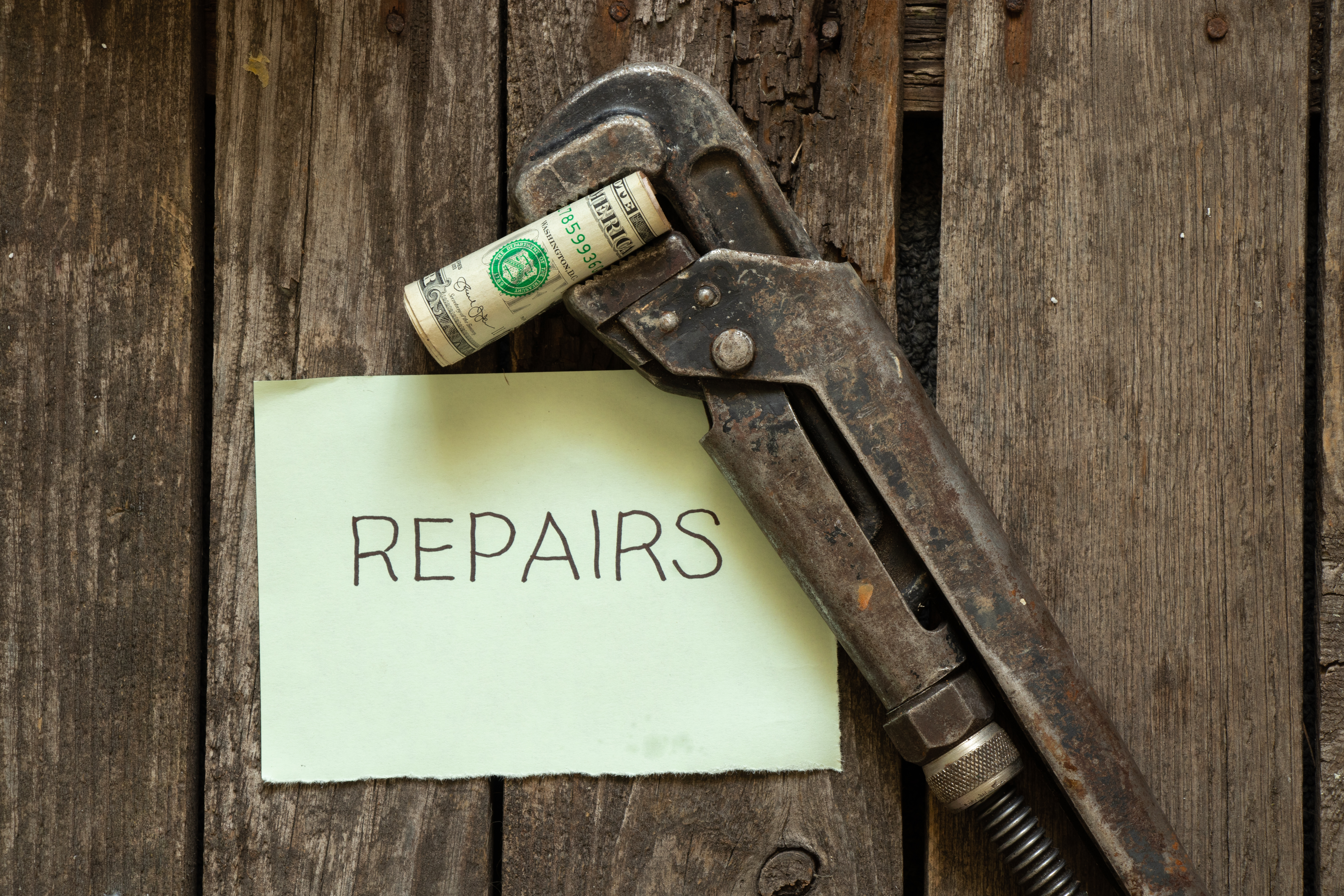 A wrench with a wad of dollars next to a paper sign that says repairs 