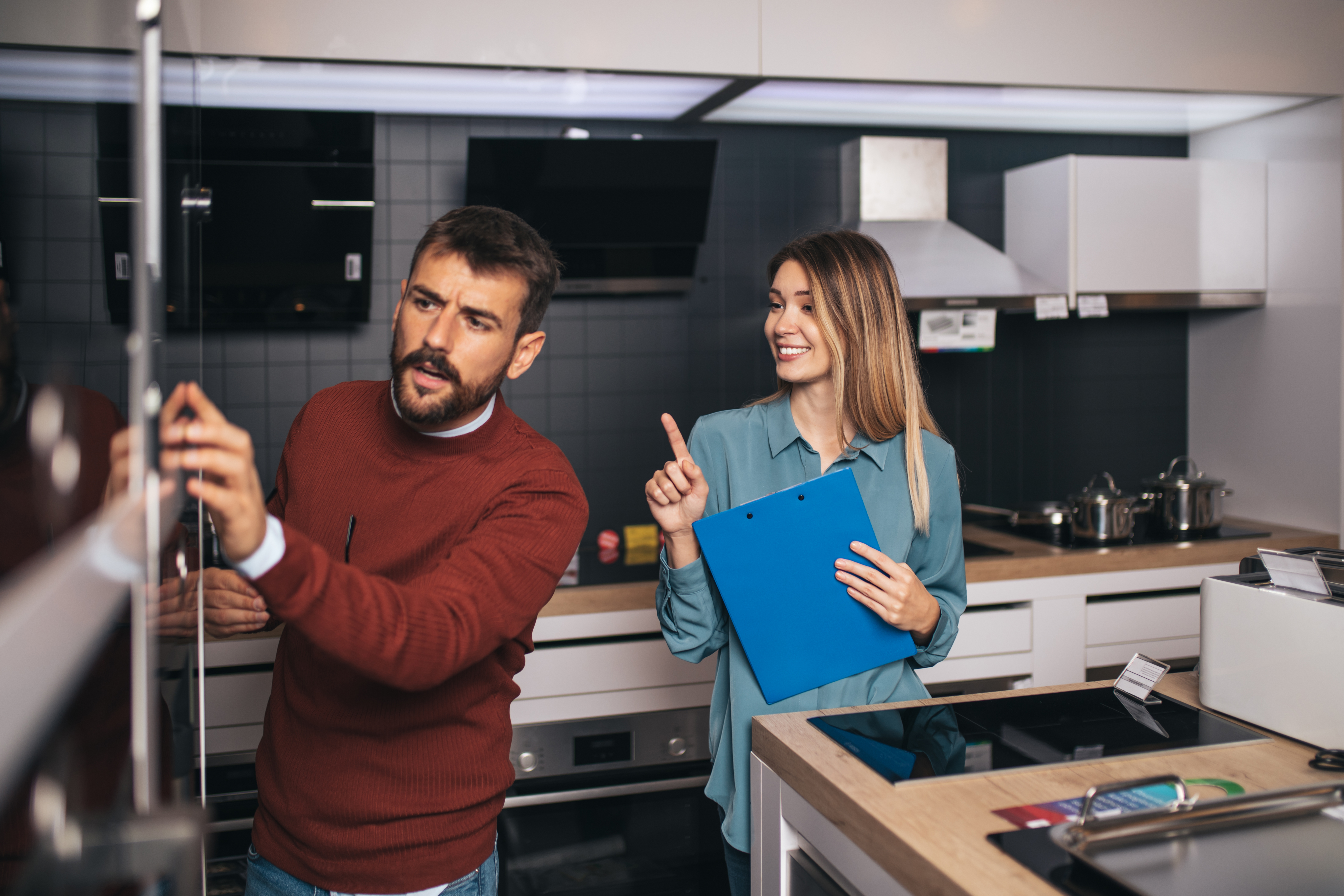 A man inspecting a fridge while an associate speaks 