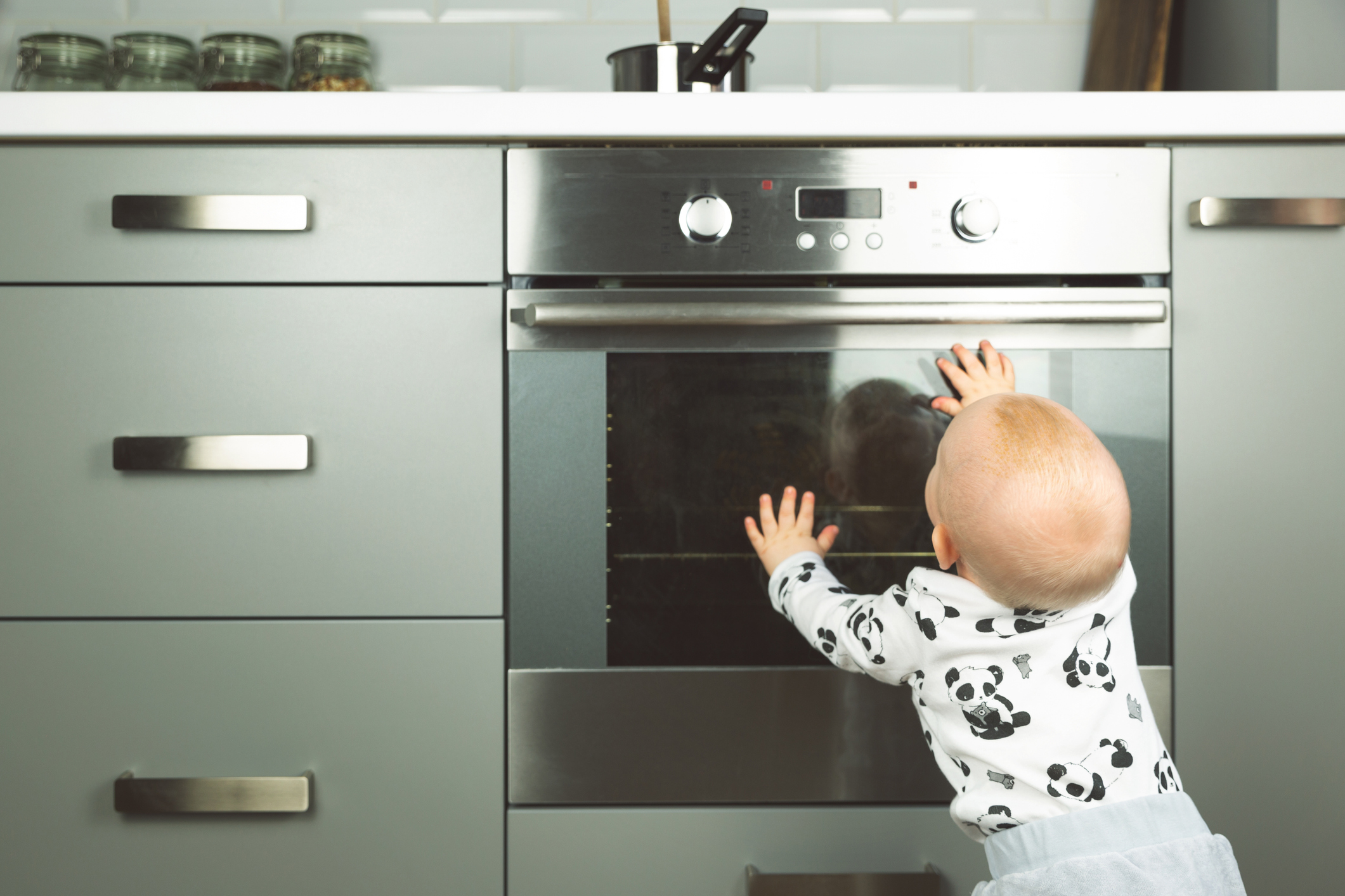 A baby touching the outside of an oven door 
