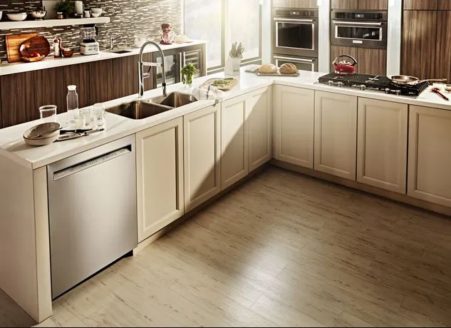 A dishwasher is seen installed into a cabinet in a kitchen with multi color cabinets and multiple appliances