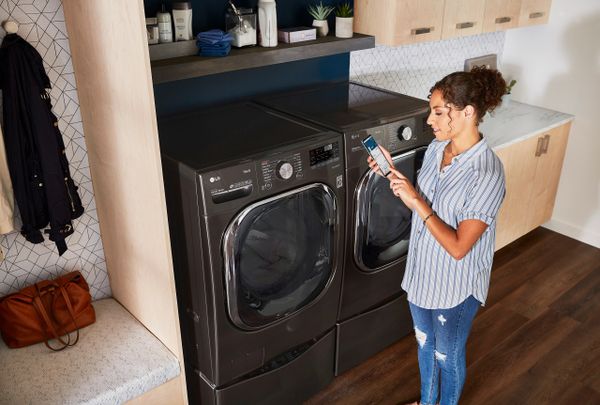 A woman uses her smart phone to check the settings on her smart washer and dryer