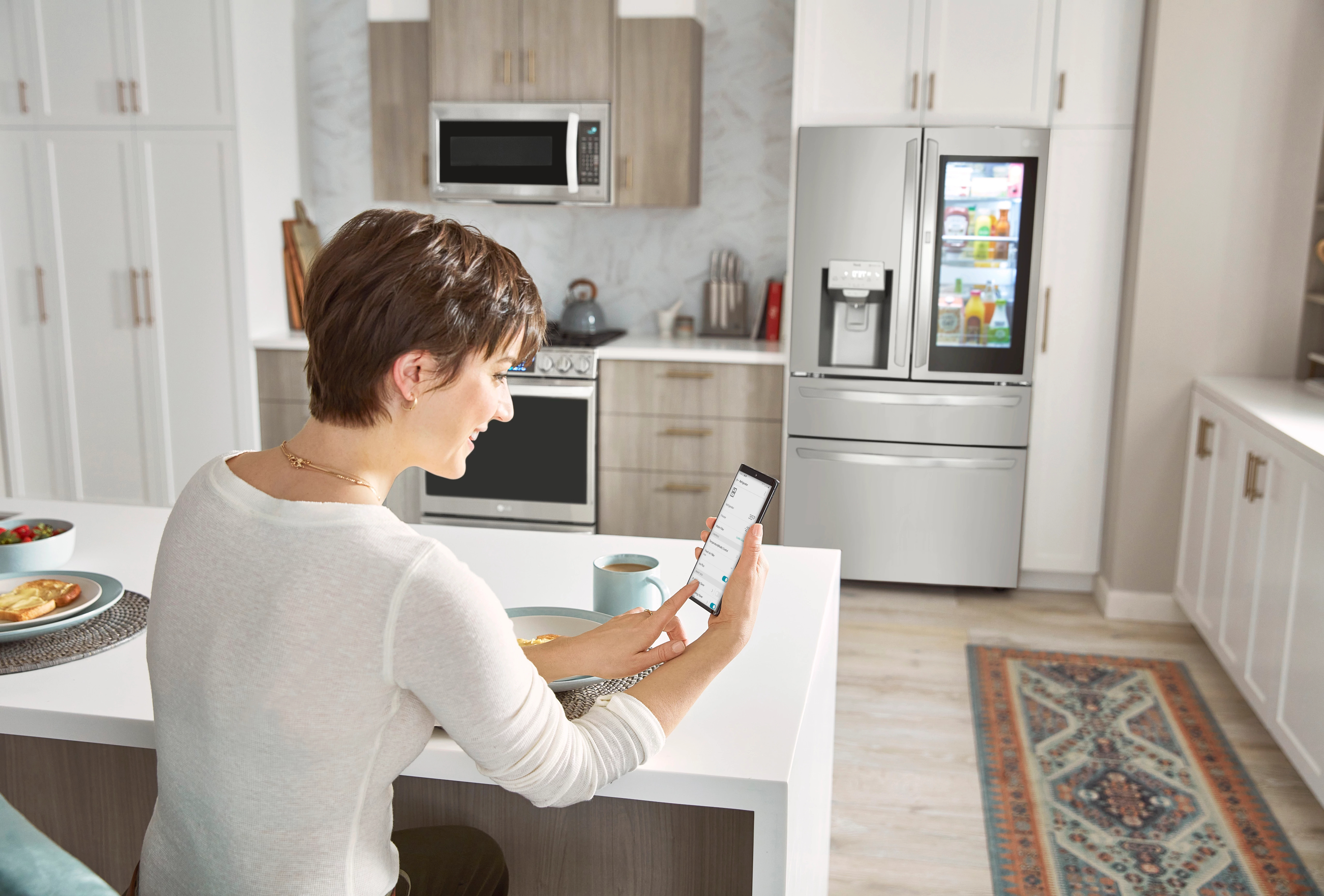 Woman checking smartphone in modern kitchen with LG refrigerator in the background.