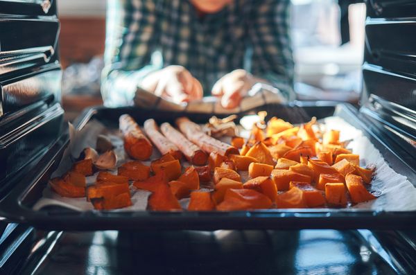 A person removing carrots and sweet potatoes from an oven 