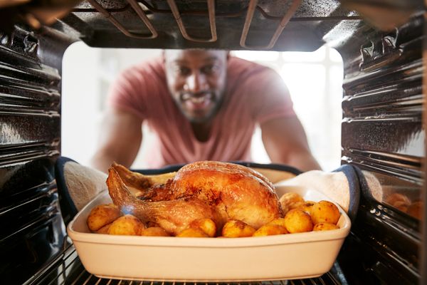 A man grabbing a roast chicken from an oven 