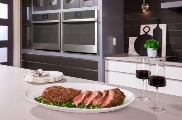 A platter of steak on counter with two GE Profile ovens in the background