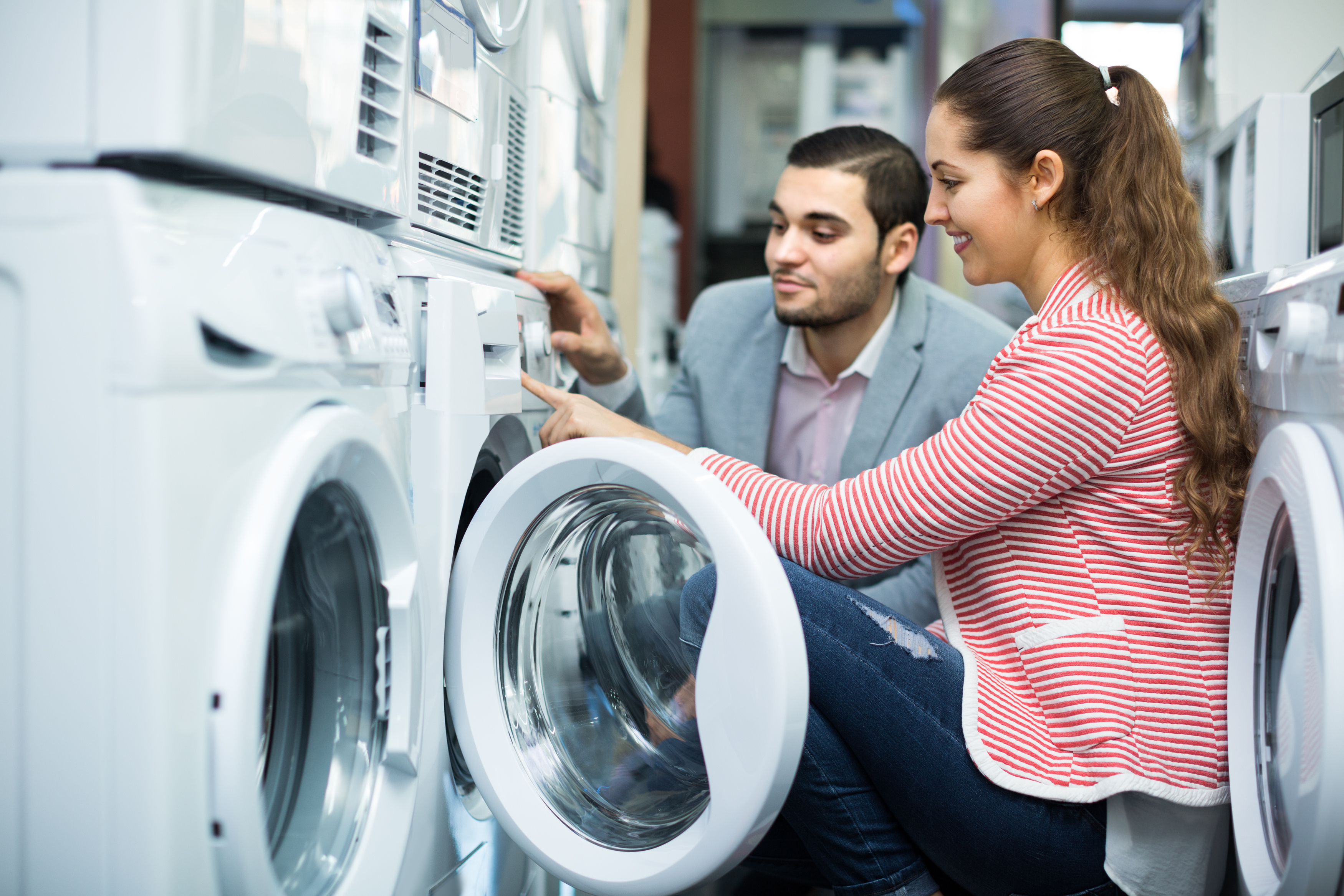 A woman smiling while testing a front load washer with a sales rep beside her 