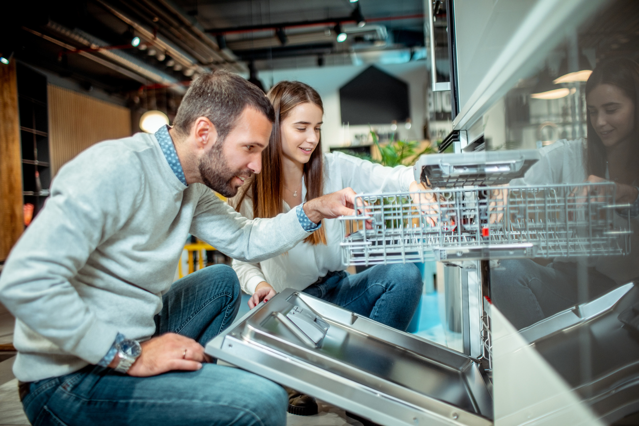 A man and a woman inspect a dishwasher in an appliance showroom