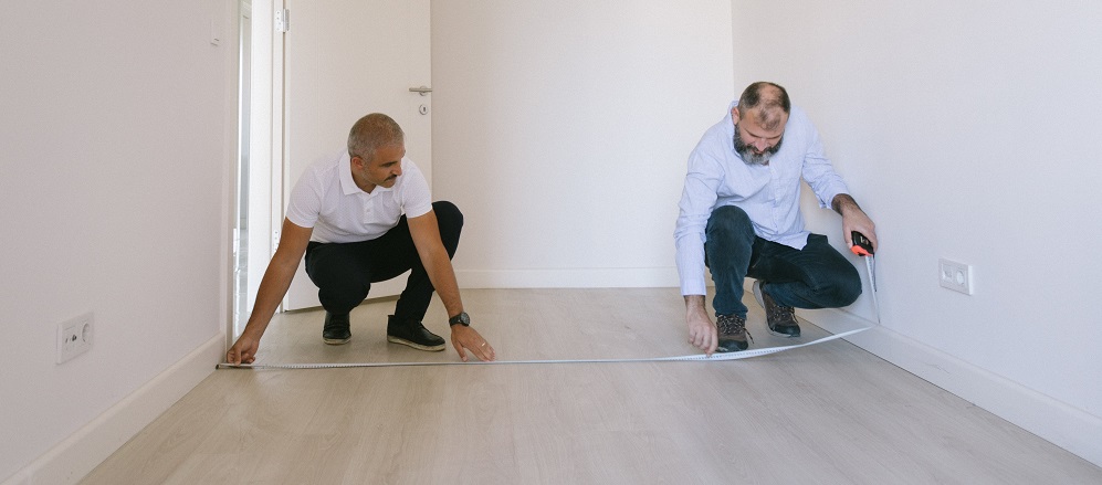 Two men using a tape measure to measure the floor 