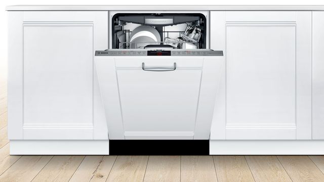front view of white kitchen cabinetry with a white panel ready dishwasher slightly opened
