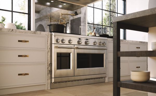view from the floor looking up at a monogram range in a modern, luxurious kitchen featuring gold accents, white cabinets, and marble countertops.
