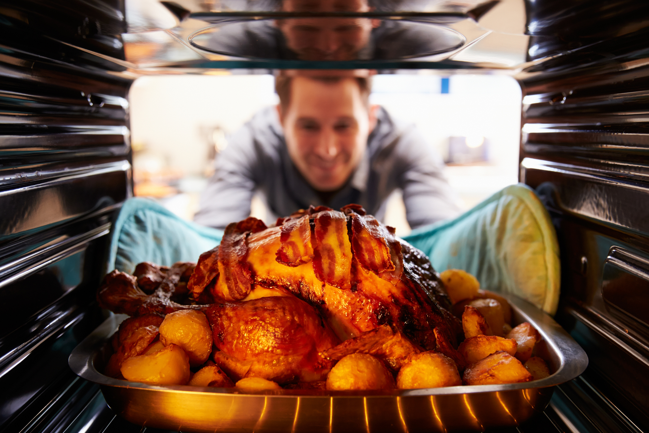 Man looking in oven with a baking turkey and fixings