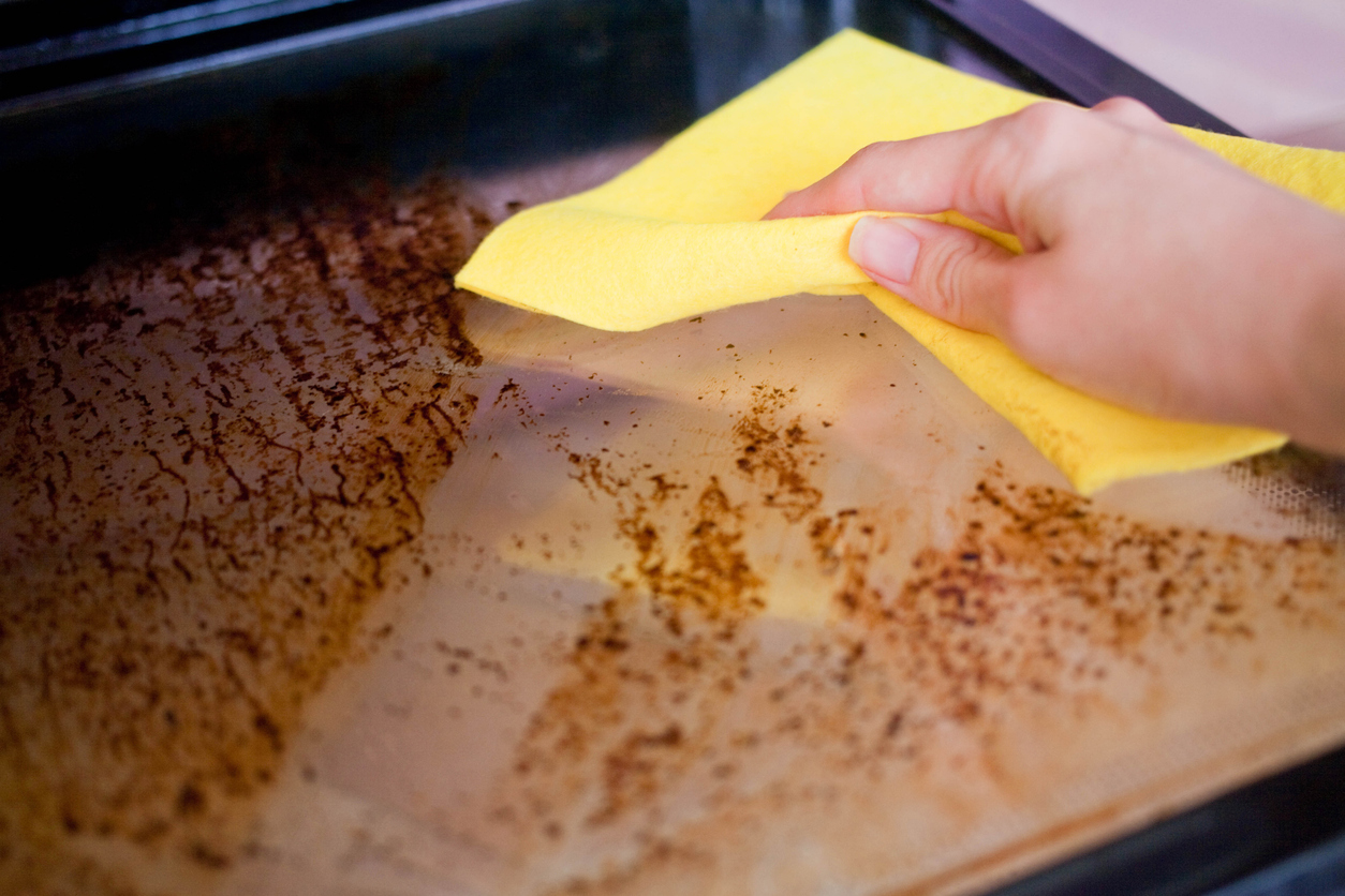 a hand wipes grease buildup off an oven door 