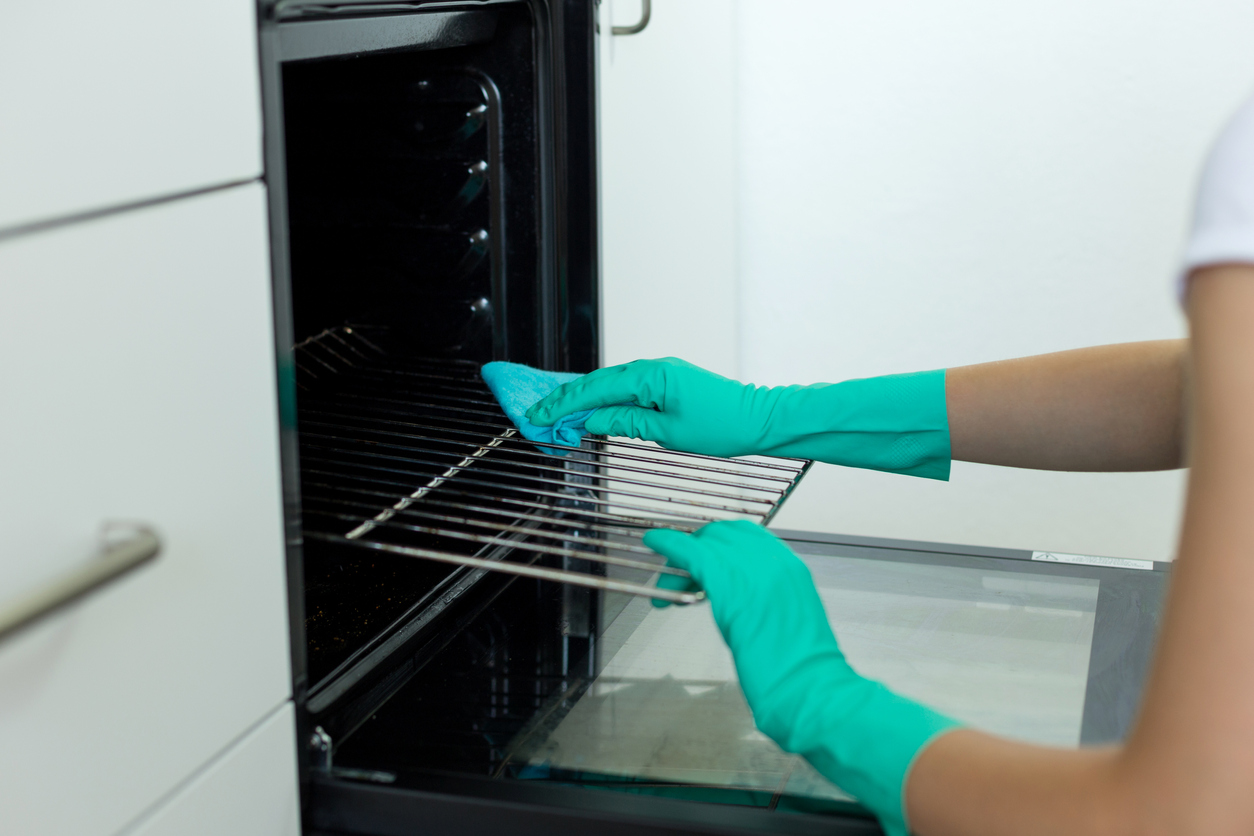 person in rubber gloves cleaning their oven racks