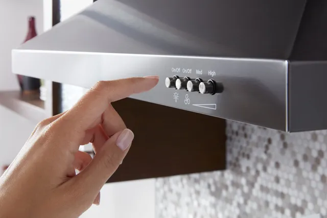 A person using the controls on the KitchenAid WVW53UC0HV black stainless range hood 