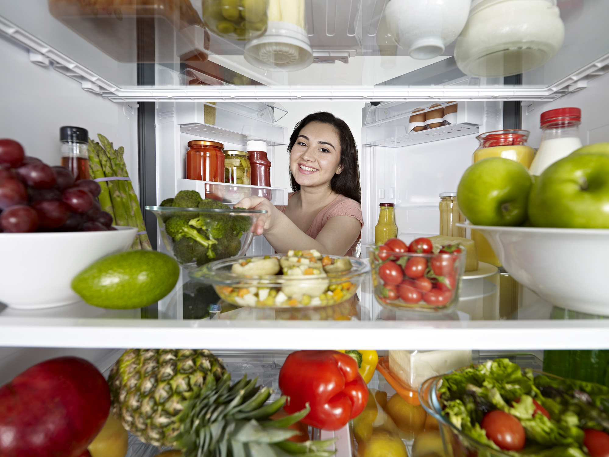 A woman reaching into a refrigerator stocked with fruits and vegetables 