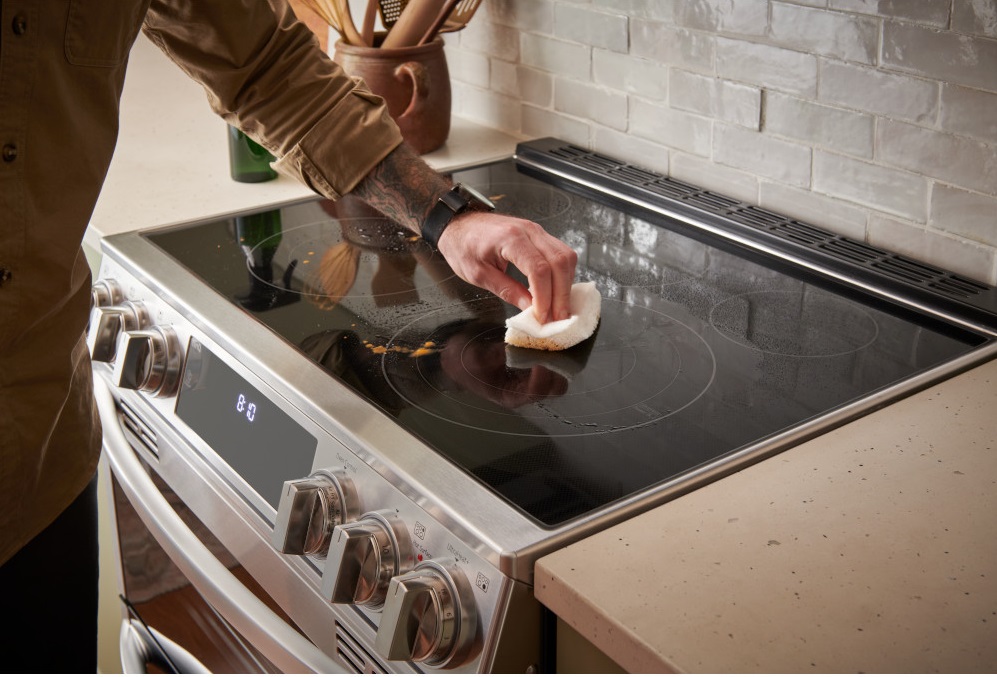 A person cleaning the top of an LG slide in electric range 