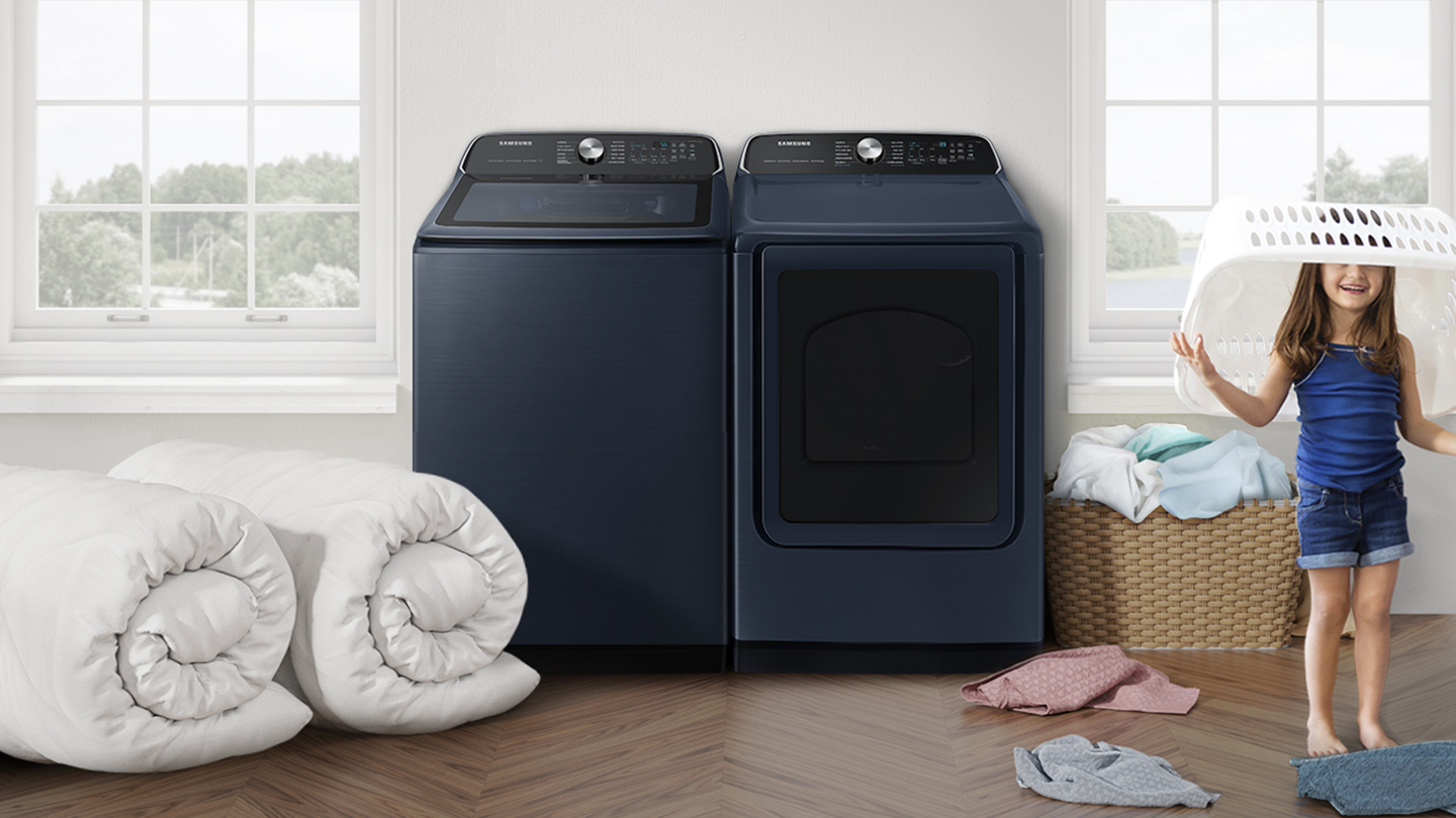 A child with a basket over its head in front of a matching Samsung top load washer and dryer
