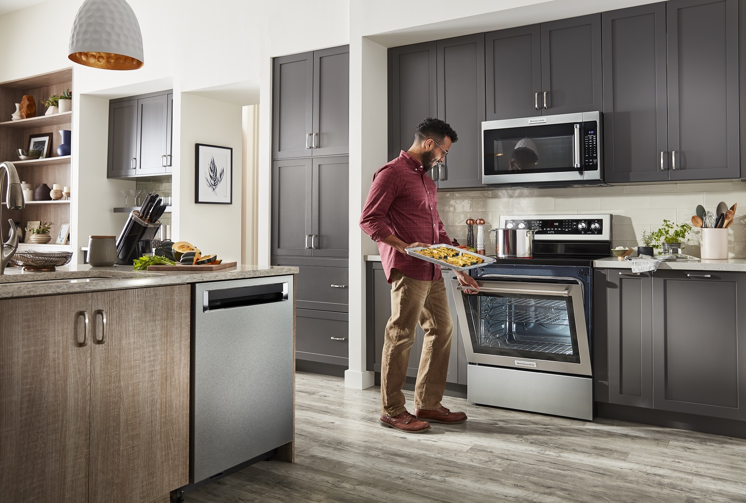 man places unbaked dish in KitchenAid oven range with KitchenAid dishwasher in view