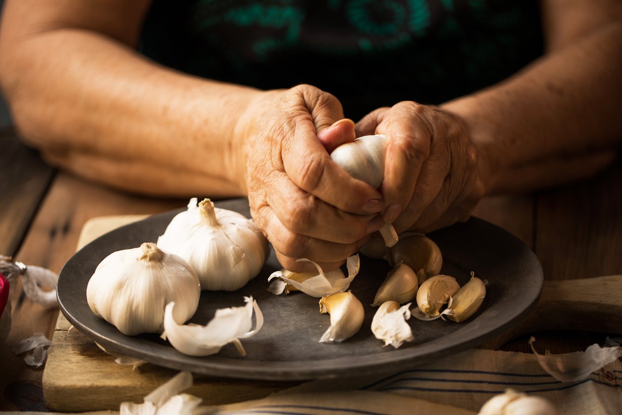 close-up of a woman’s hands removing garlic skin over a plate
