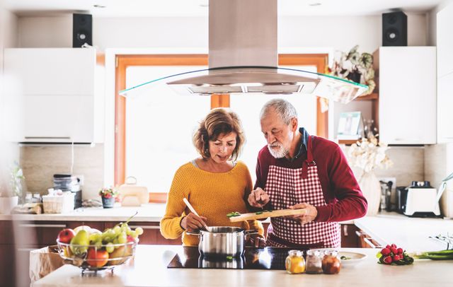 front view of a couple cooking dinner under a stainless teel island range hood