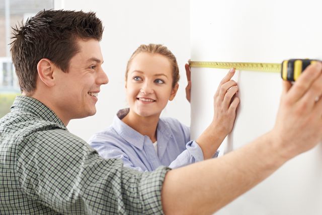 a man and a woman measuring a wall in a kitchen
