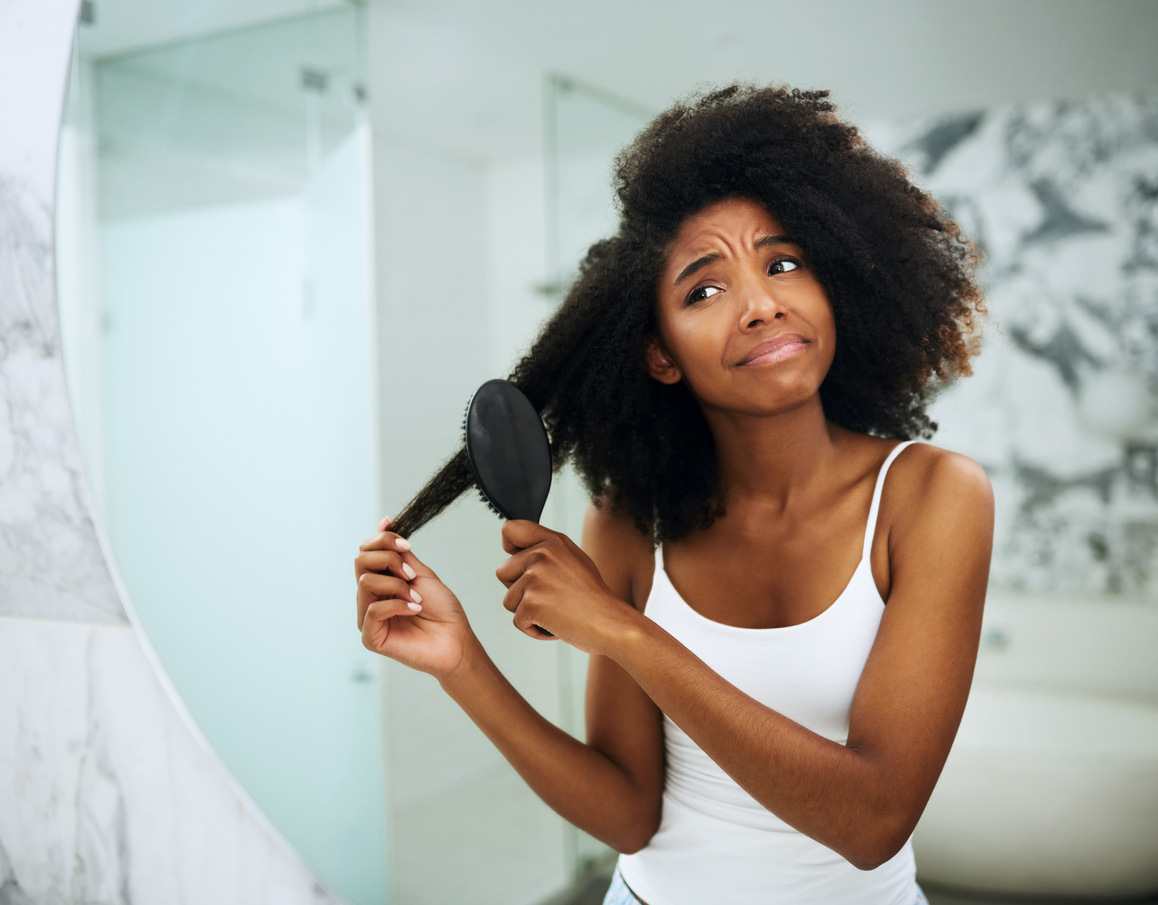 young woman struggling to comb her hair at home