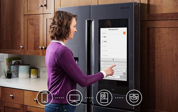 A woman uses a smart refrigerator to make a grocery list
