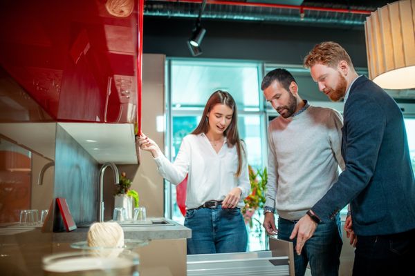 An appliance salesman demonstrating a product to a man and a woman 