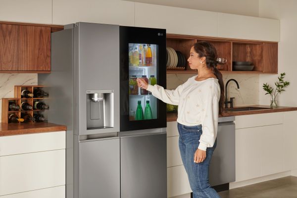 A woman using the InstaView feature on the LG LRSOS2706S refrigerator