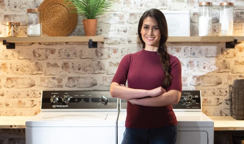 woman smiles proudly in front of her Speed Queen washer and dryer set
