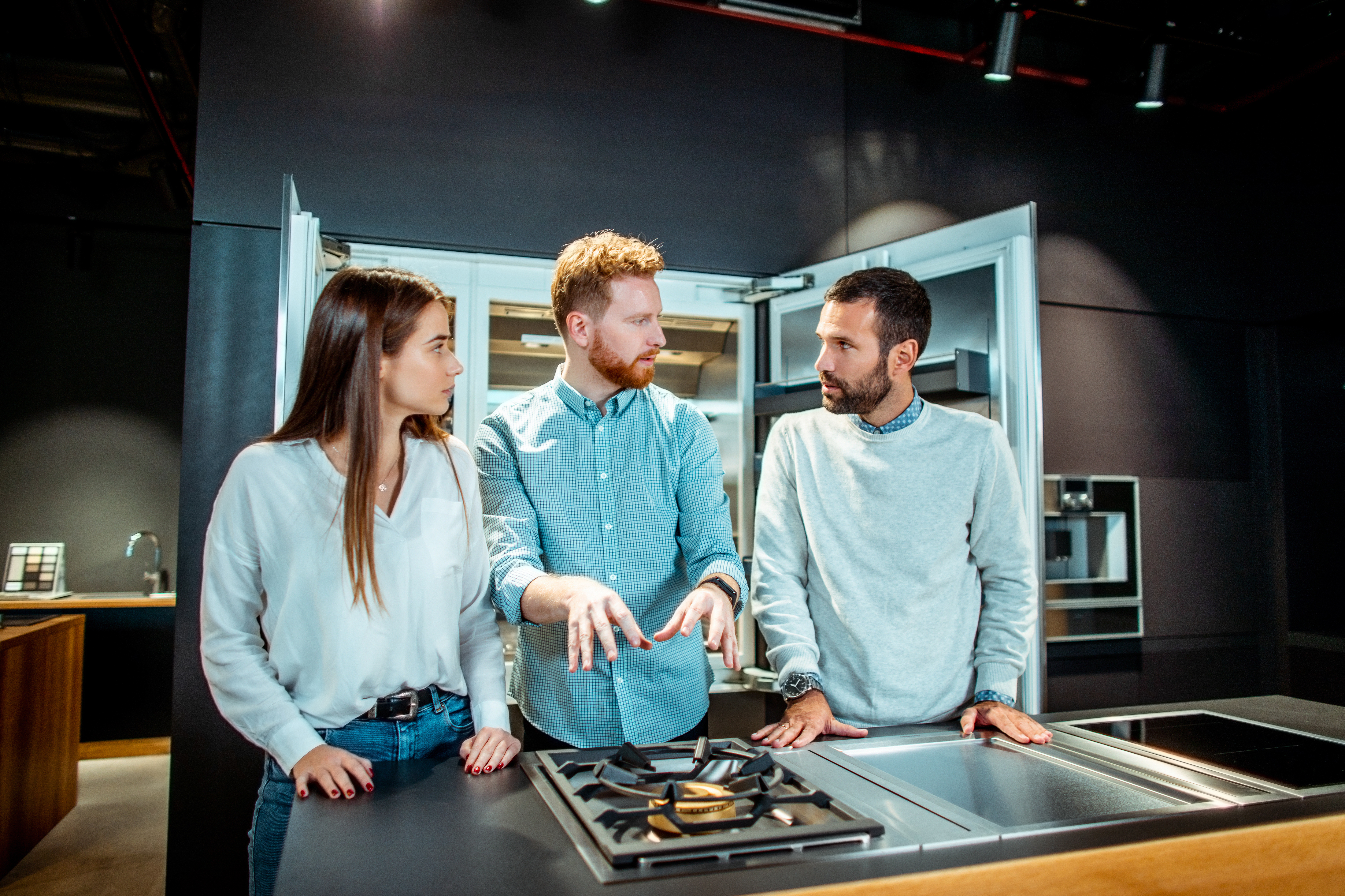 A man describing a gas cooktop to a man and a woman 