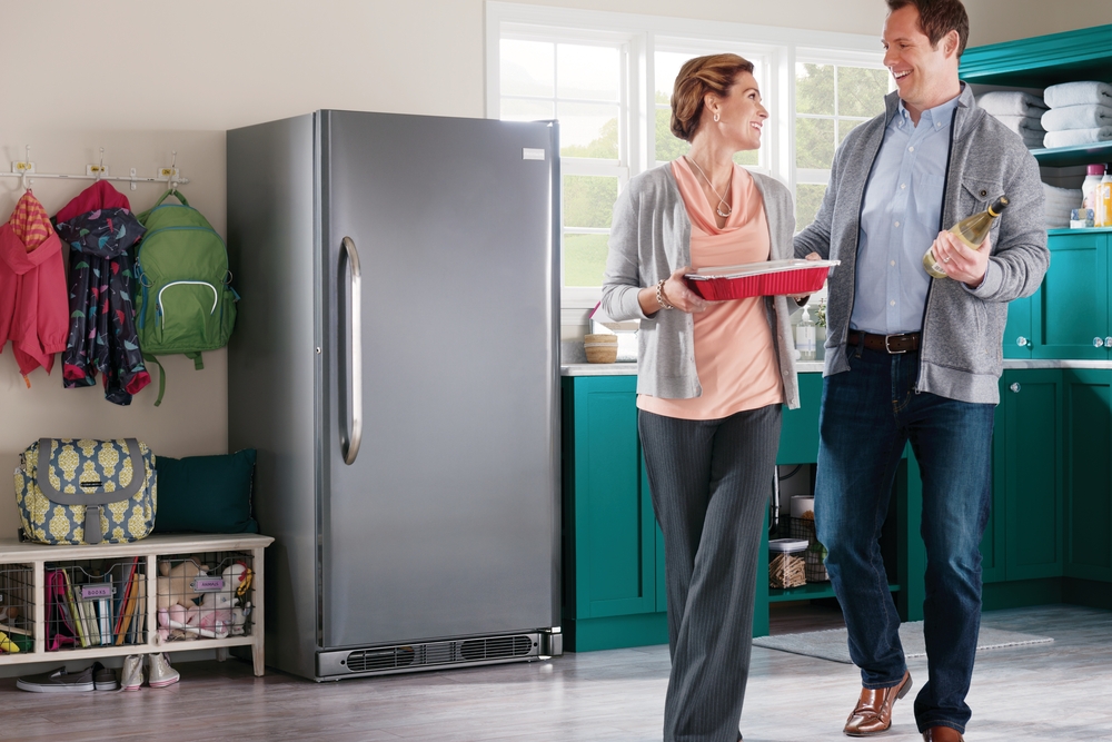 Middle aged man and woman smiling with an upright freezer in the background