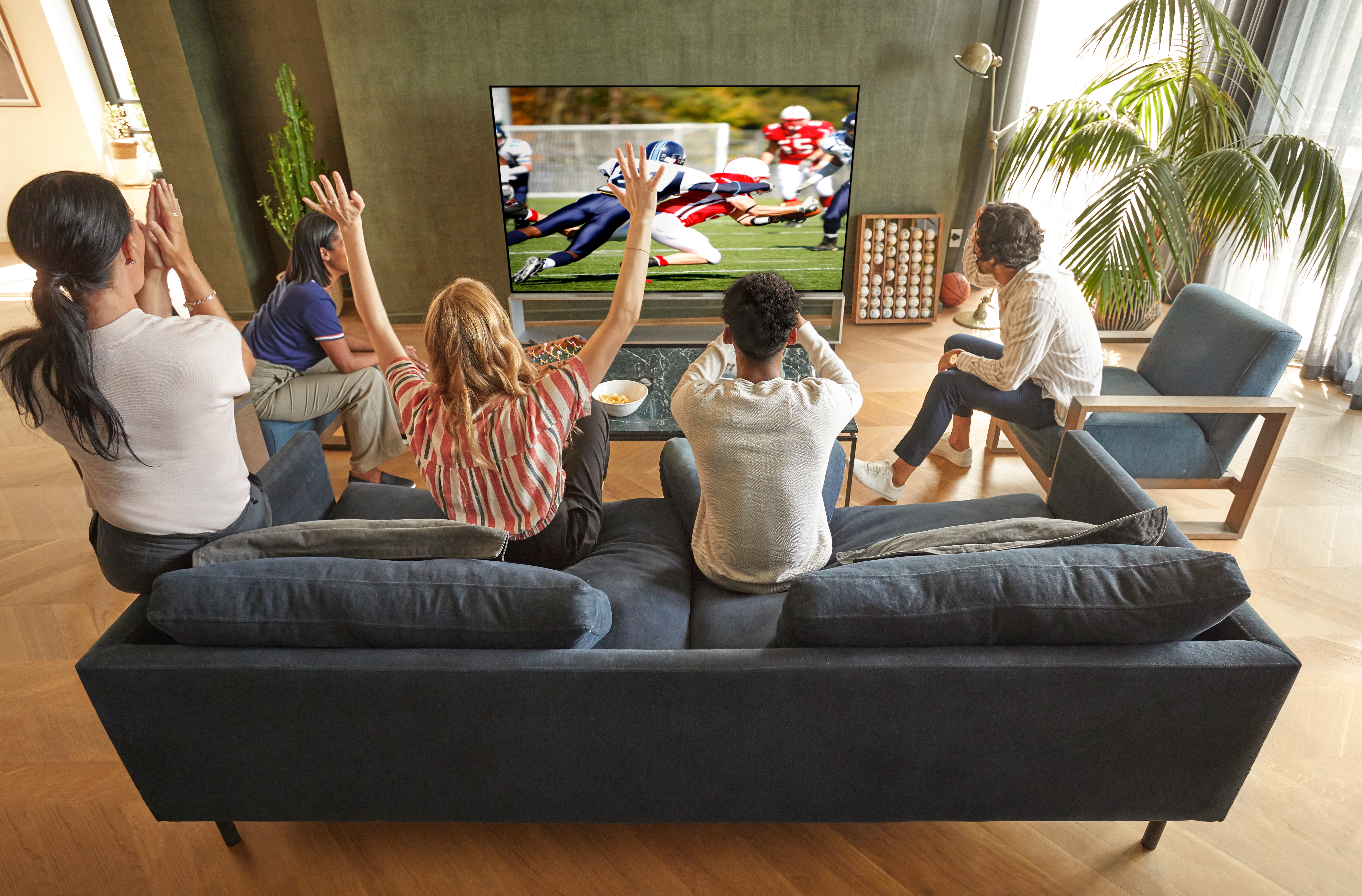 A group of adults sit and watch American football on LG OLED TV