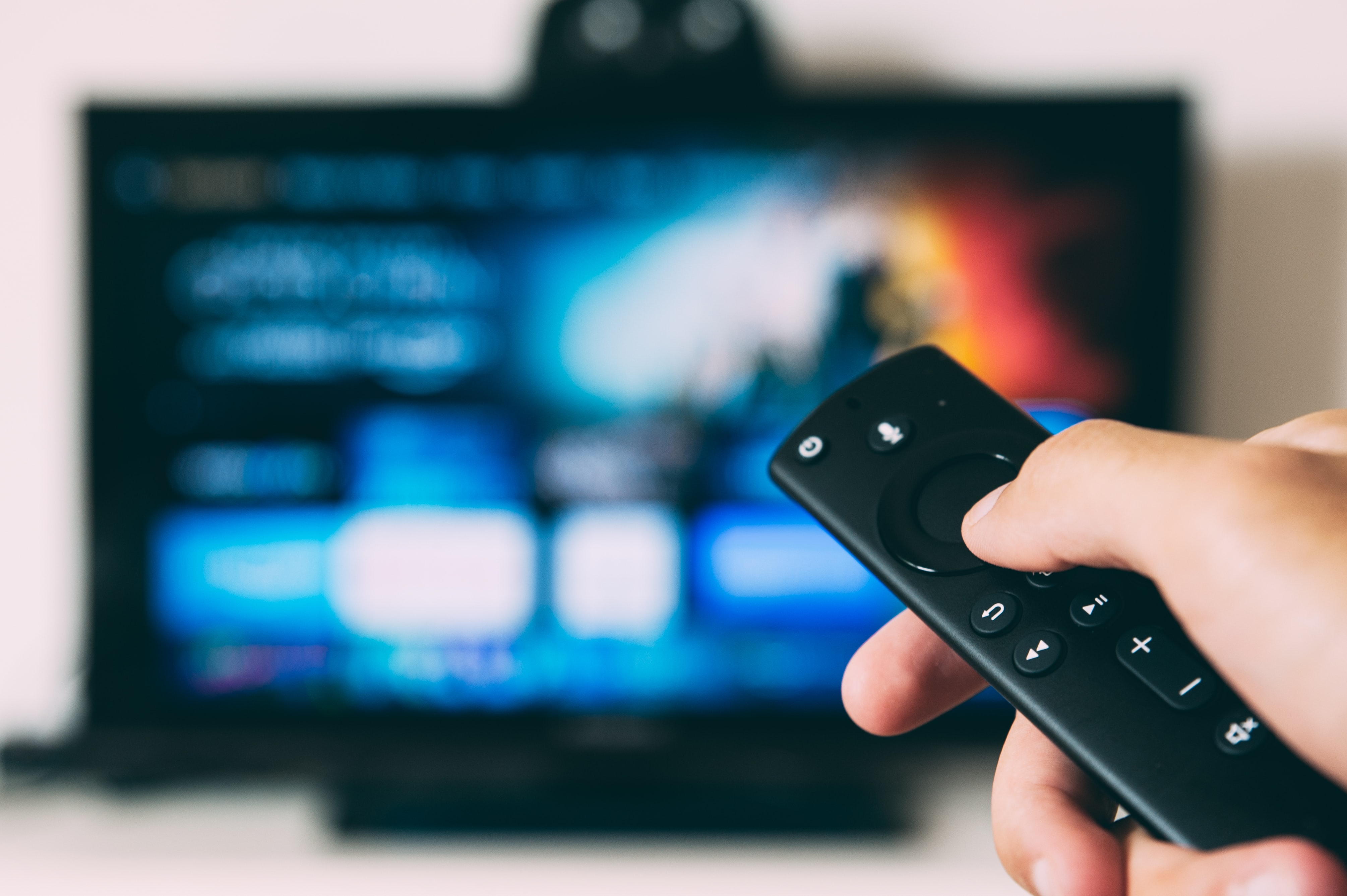 Close up of a remote with a blurred TV in the background 