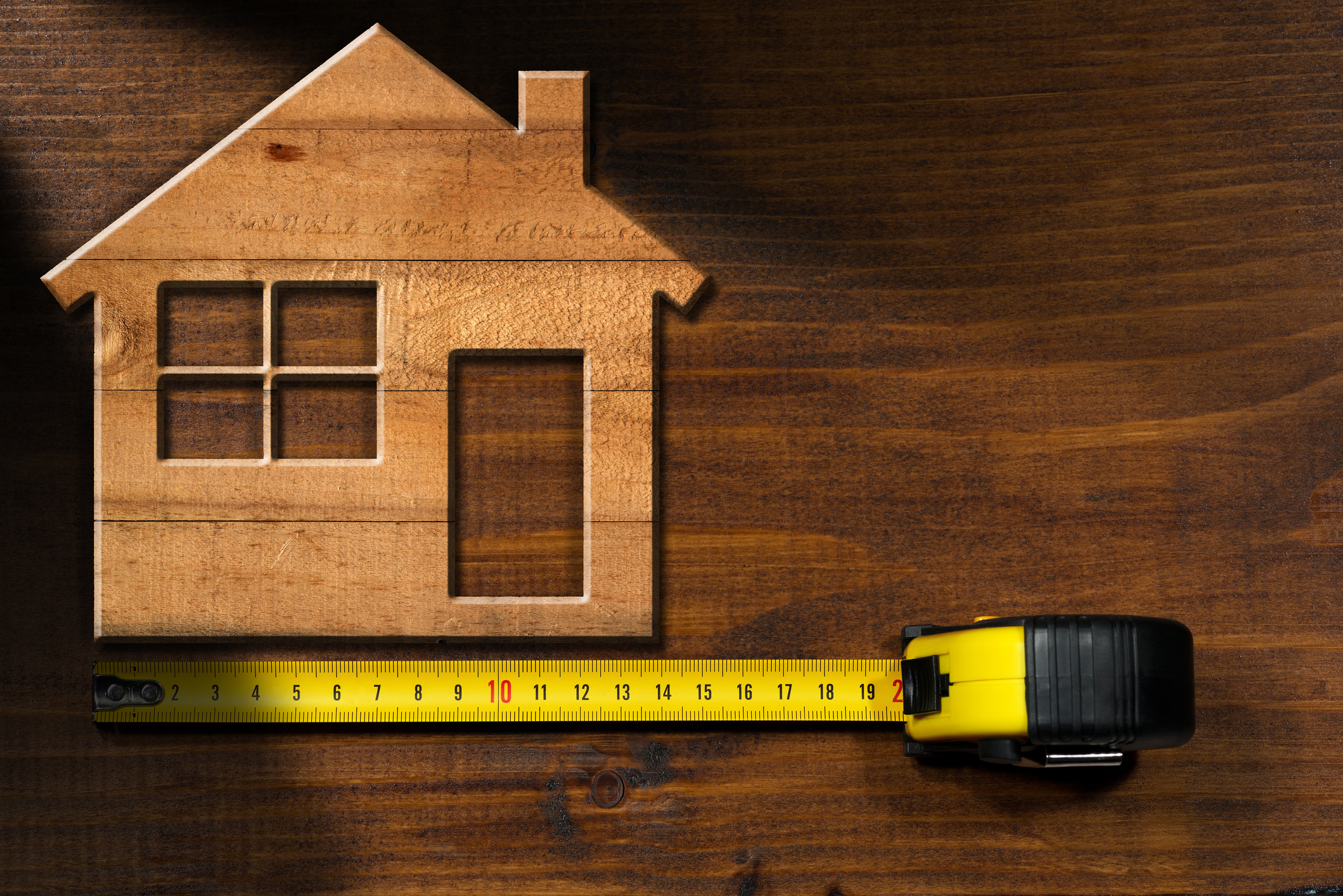 Wooden cutout of home on a wooden tabletop next to an extended tape measurer