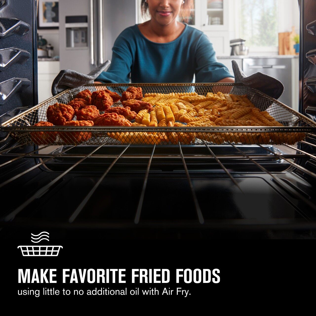A woman taking wings and fries out of an oven 